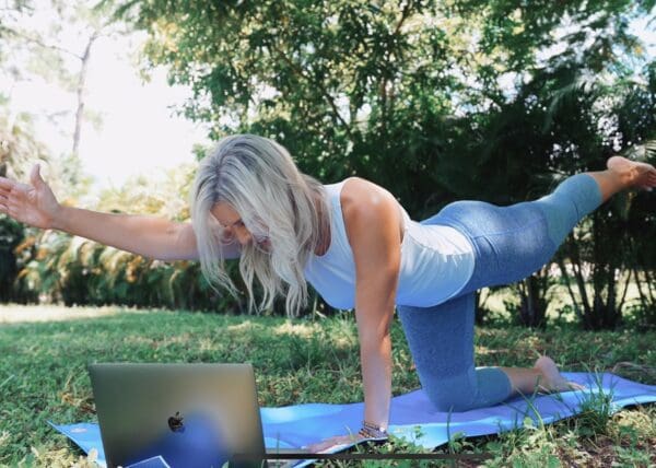 A woman doing yoga outdoors with a laptop